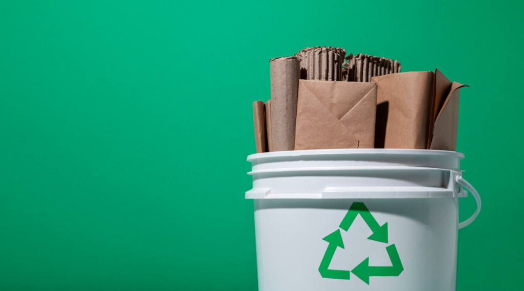 Recycling container with cardboard items in front of green wall